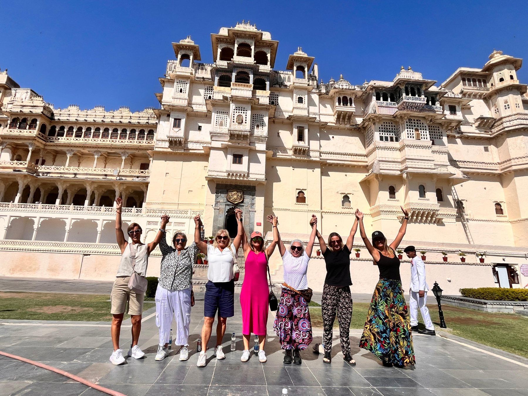 Grupo de viajeras con los brazos en alto frente a un palacio de India